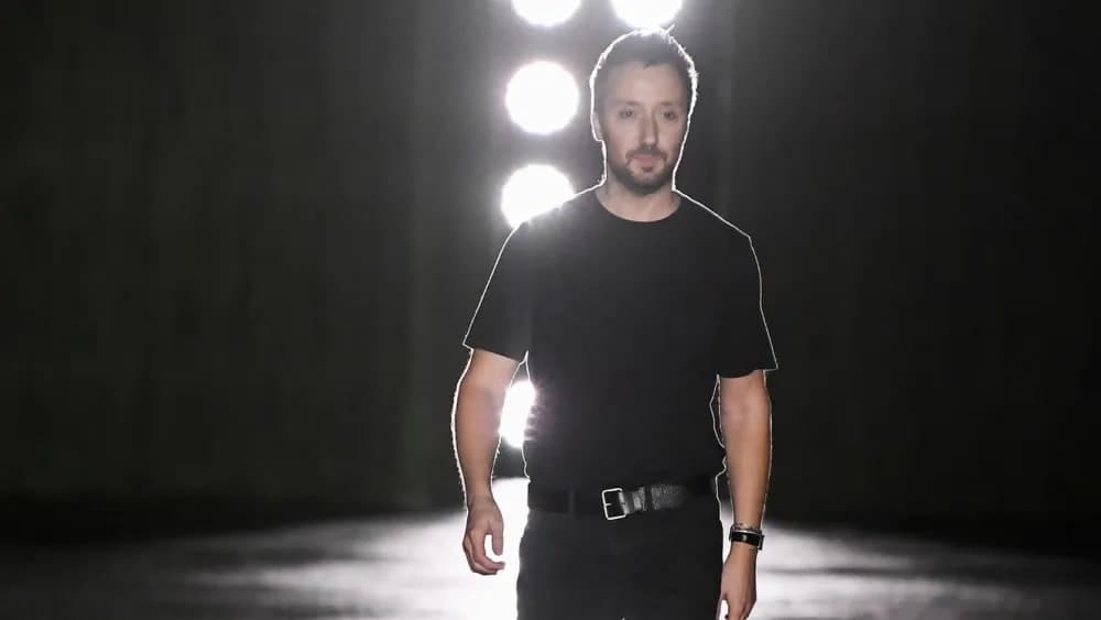 Anthony Vaccarello walking out for his runway bow at a Saint Laurent show, backlit by stage lights
