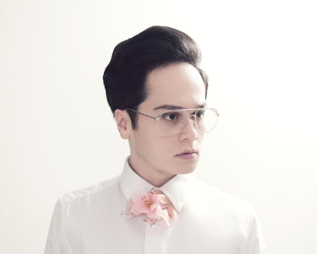 Bassi Lichtenberg in profile wearing glasses and a white shirt with a pink flower boutonniere, against a white backdrop
