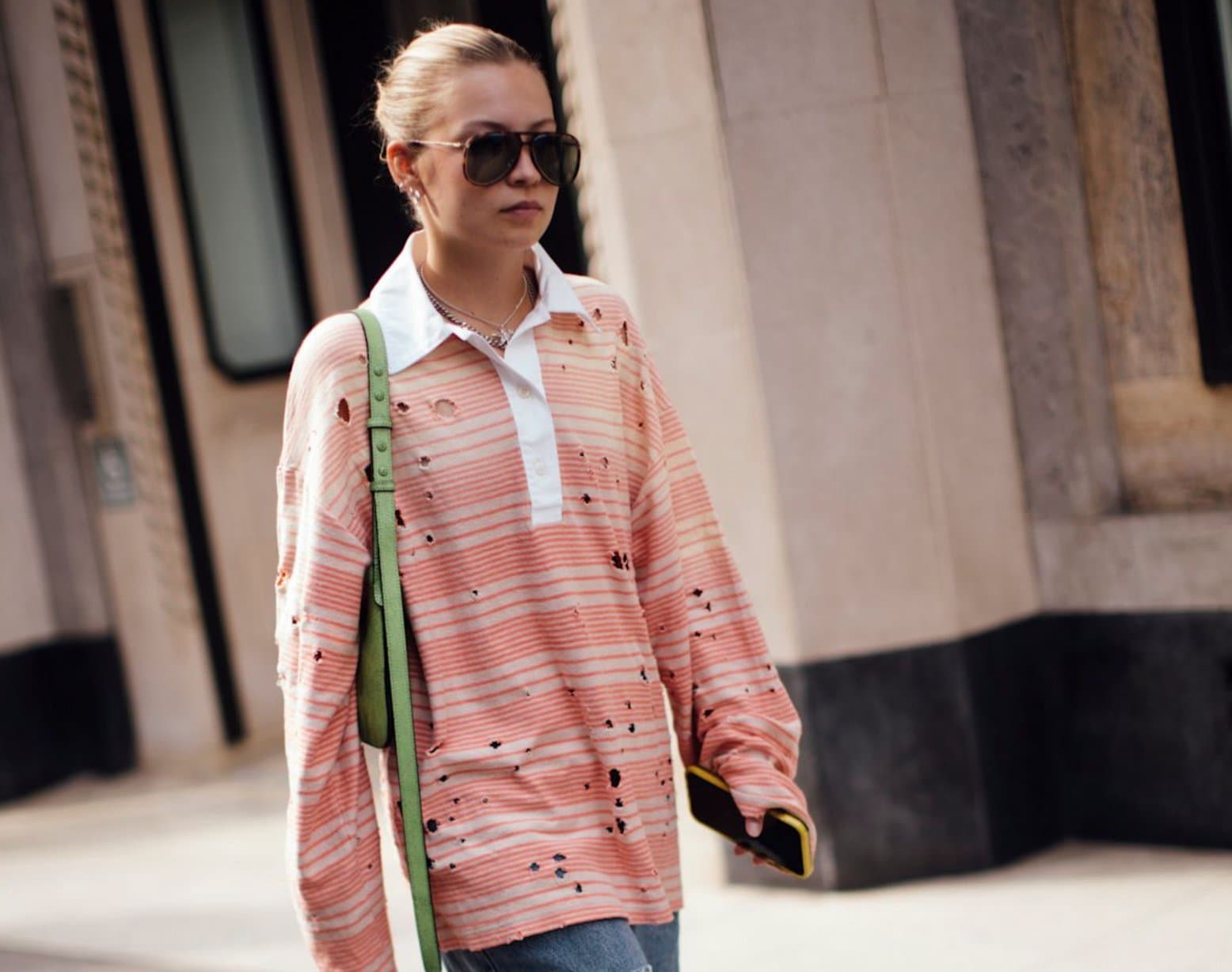A woman in sunglasses wearing an oversized distressed striped popover shirt with a white collar and a green crossbody bag