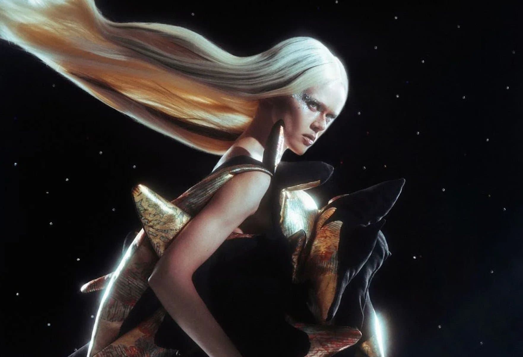 A model in an ethereal gold and black cosmic-inspired gown with wind-swept pale hair against a starry backdrop