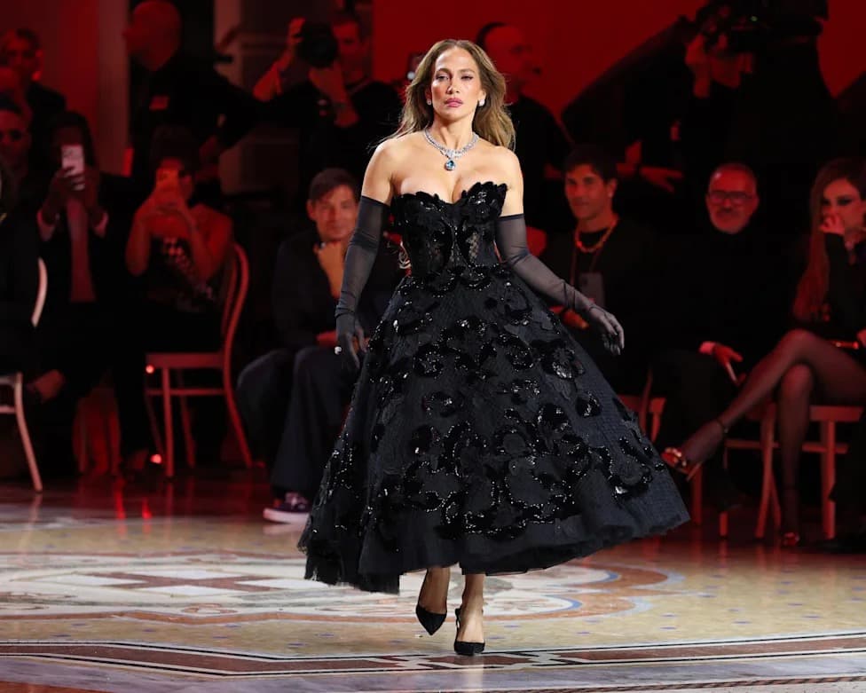 A model walking the Dolce & Gabbana runway in a black strapless tulle gown with sequined floral appliqué, opera gloves, and a statement necklace