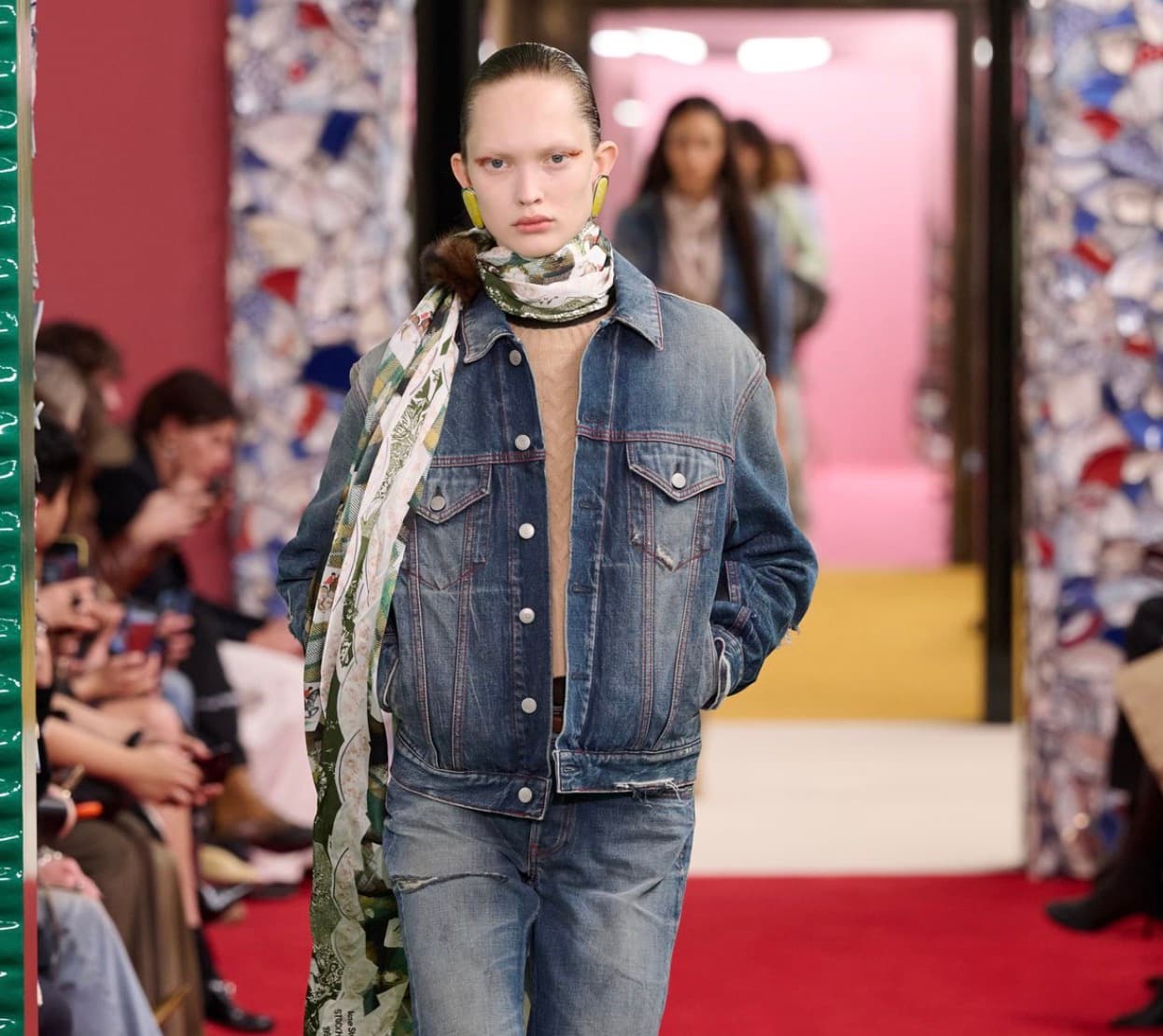 Model on a runway wearing an oversized denim jacket, denim jeans, and a printed scarf
