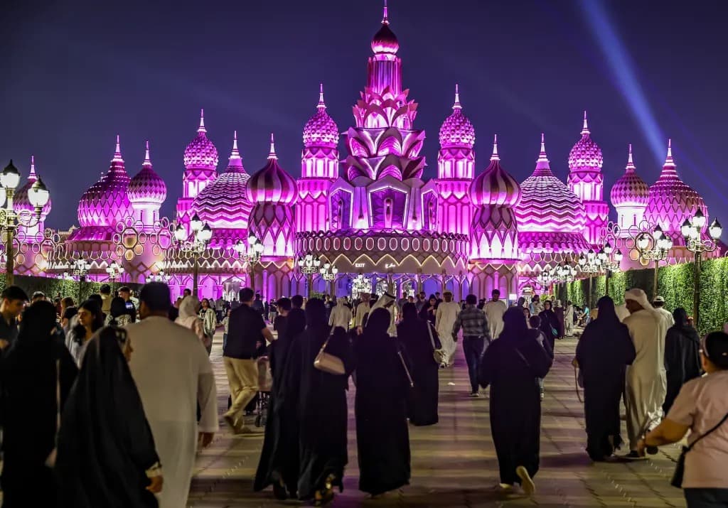 Crowds walking toward the illuminated purple onion-domed entrance of Global Village in Dubai at night