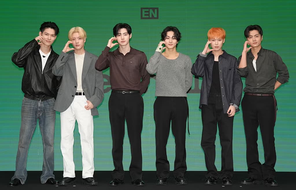 The seven members of K-pop group ENHYPEN posing together on stage in front of a green backdrop with the group's logo