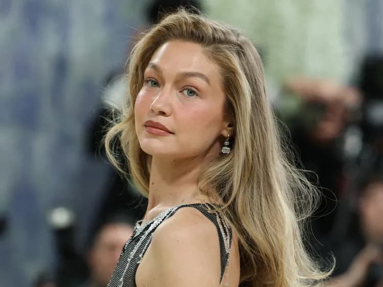 Close-up of Gigi Hadid with long wavy blonde hair, wearing a dark sparkly top and a drop earring
