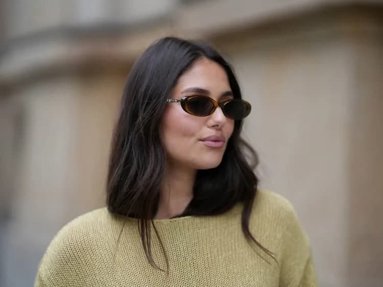 Woman with dark, naturally air-dried hair wearing tortoiseshell sunglasses and a mustard-yellow sweater