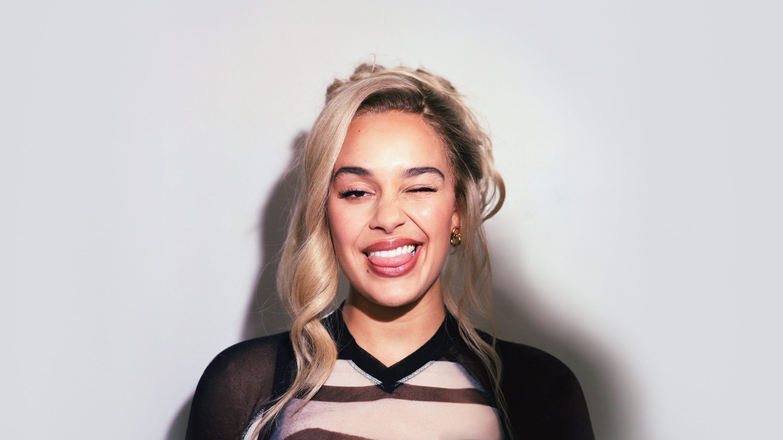 Jorja Smith laughing and winking at the camera against a plain grey background