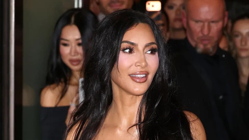 Kim Kardashian arriving at an event with dark wavy hair and a plunging neckline dress, surrounded by onlookers