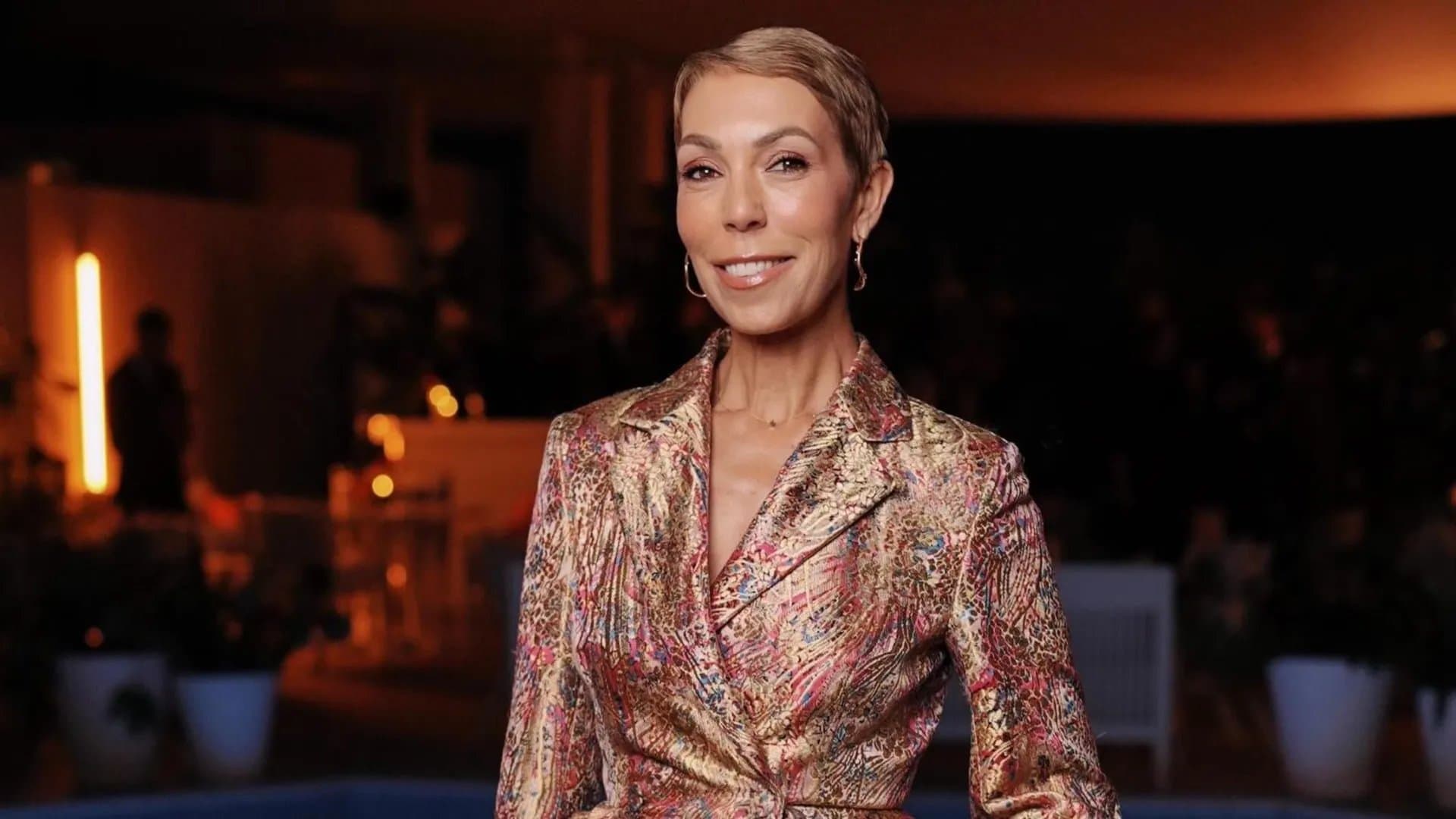 Mathilde Favier smiling in a metallic floral-print jacket at an event