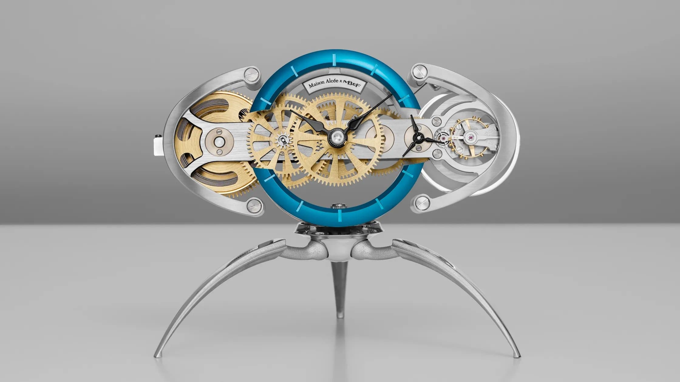The MB&F x Maison Alcée Nostromo desk clock, an oval skeletonized clock with exposed gold and steel gearing on spidery metal legs
