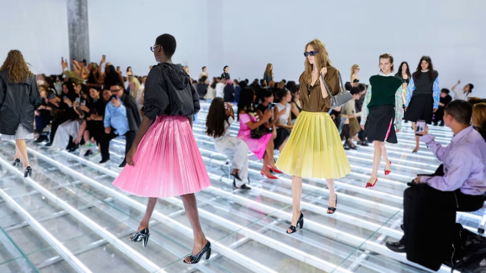 Models walking the Prada spring 2027 runway wearing pleated and embellished skirts paired with tailored jackets