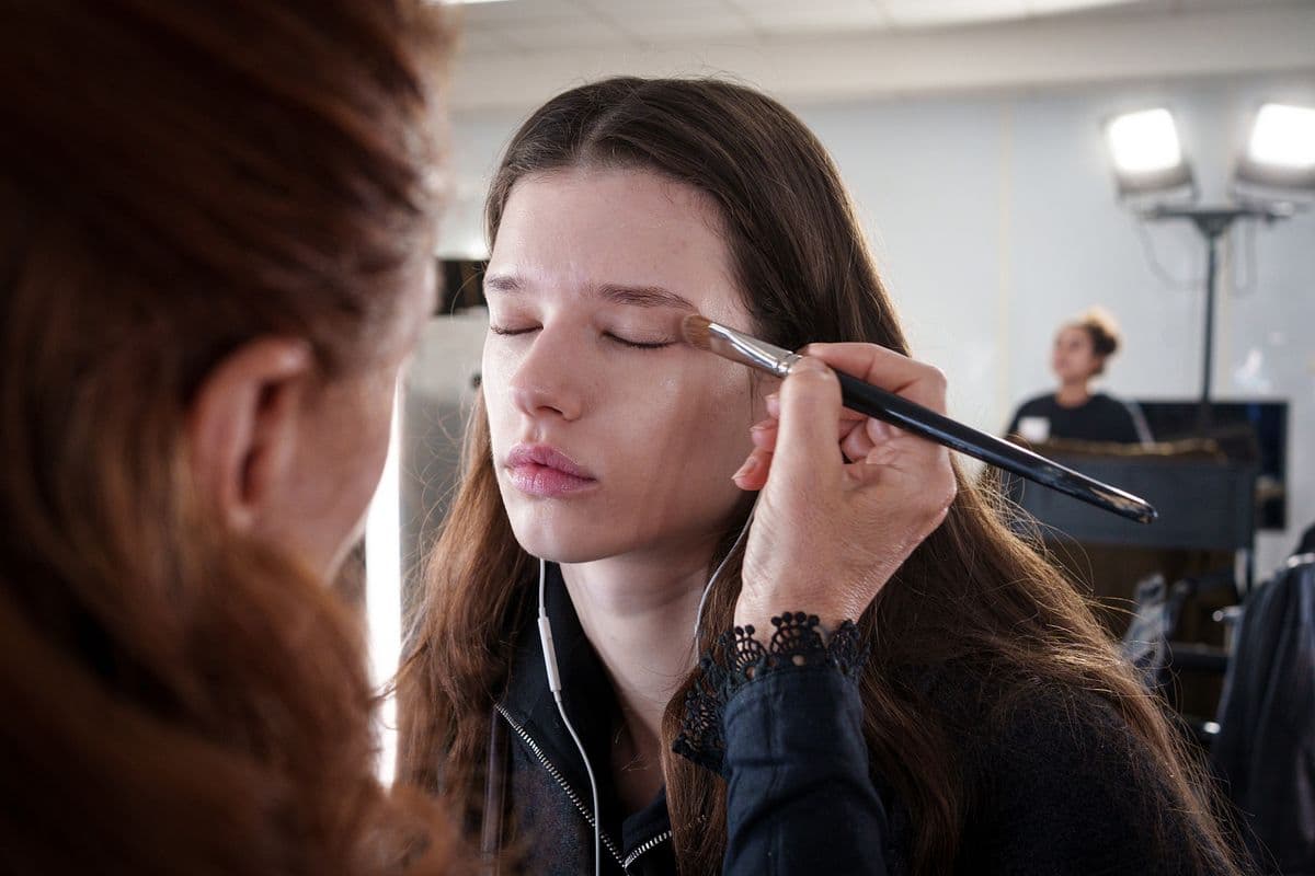 Makeup artist applying eyeshadow to a model's closed eye backstage