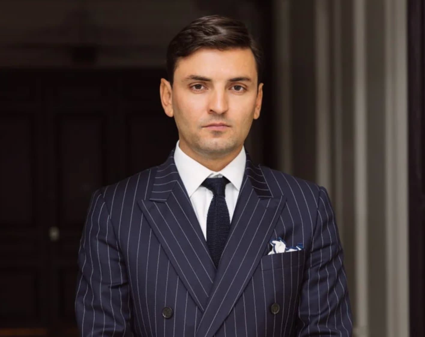 Nicolas Paganelli in a pinstriped double-breasted suit and tie, standing in a dark wood-paneled interior