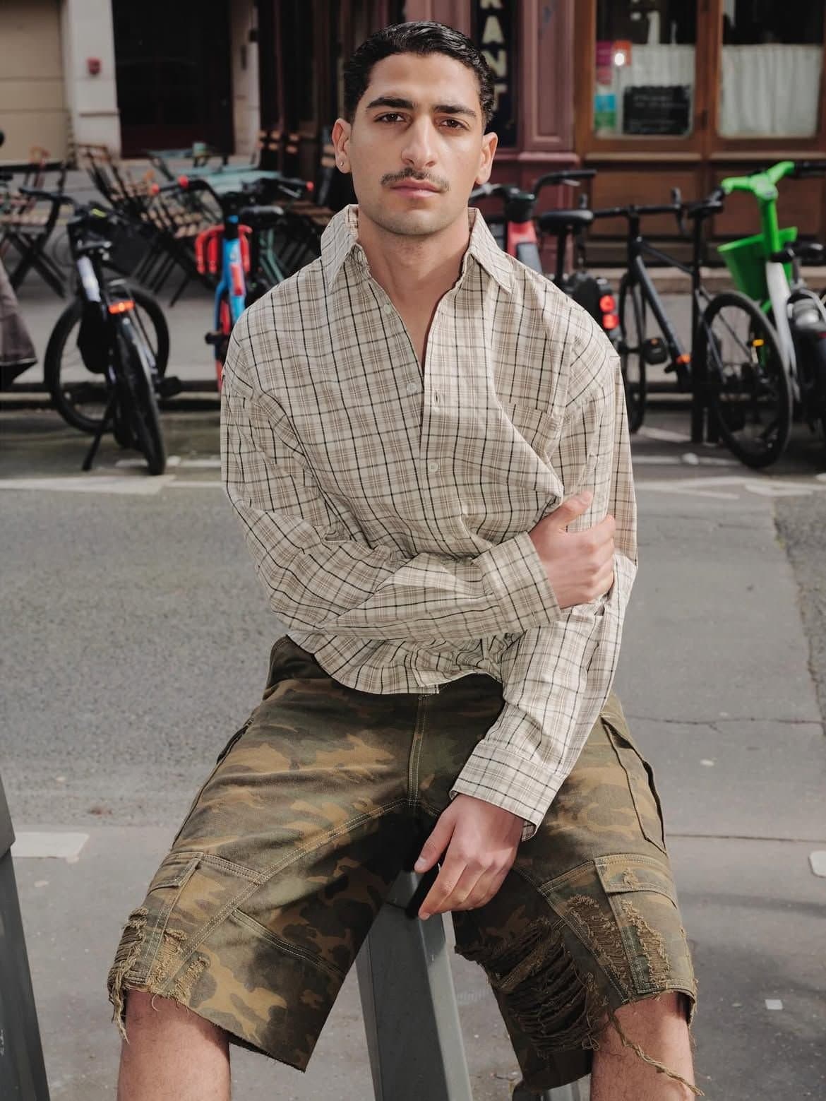A man modeling a spring/summer look pairing a checked shirt with distressed camo shorts