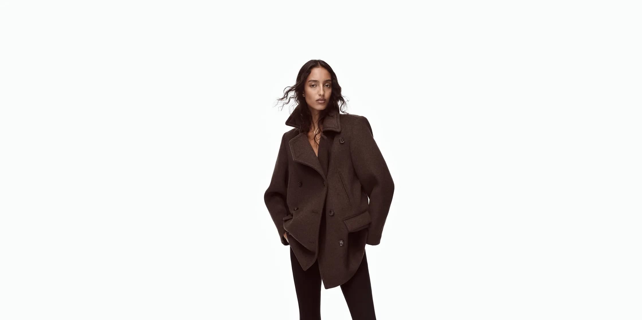 Model wearing an oversized dark brown wool double-breasted peacoat from the Victoria Beckham x Gap fall collection against a plain white background
